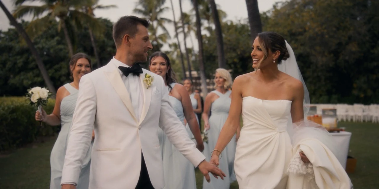 Caroline and Dylan walk hand in hand from the ceremony, smiling at one another.