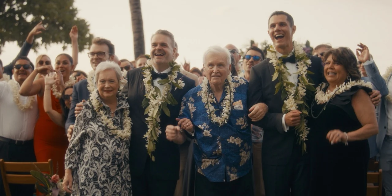 Jaime and Travis move through a cheering gathering with older guests beside them.