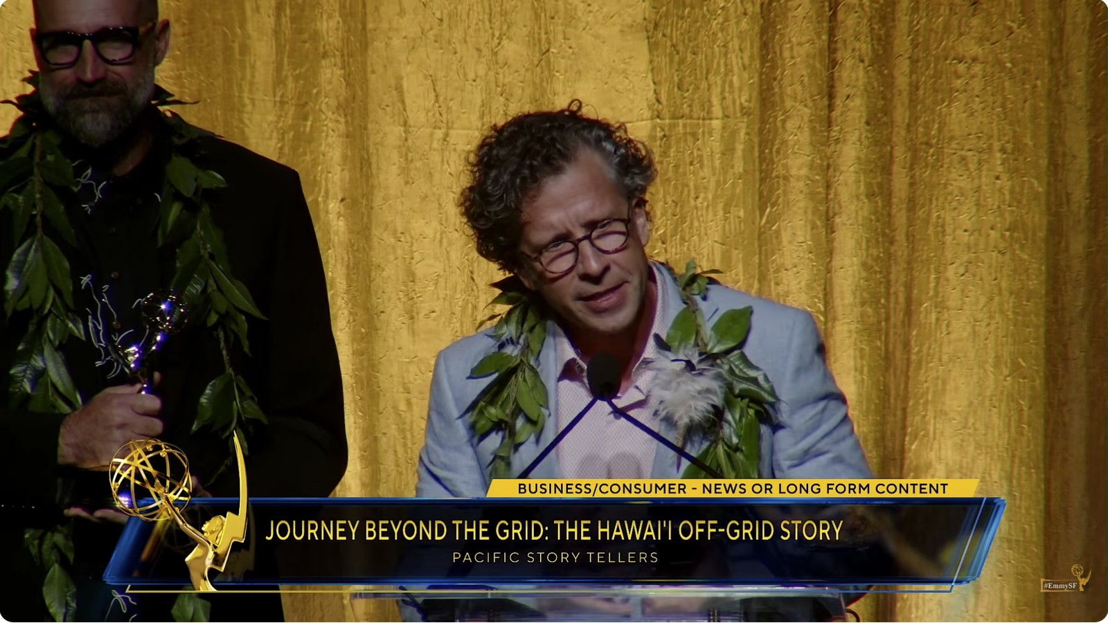 Stephan Boeker speaks while David Sellers holds an Emmy after Journey Beyond the Grid received the 2026 Business/Consumer award.